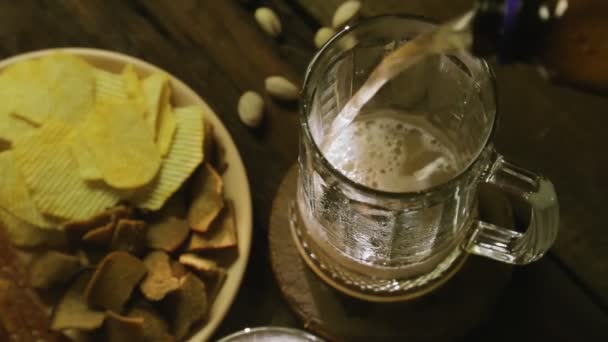 Αφρός κρύο φως μπύρα χύνεται σε κούπες σε ένα ξύλινο τραπέζι πάνω άποψη — Αρχείο Βίντεο