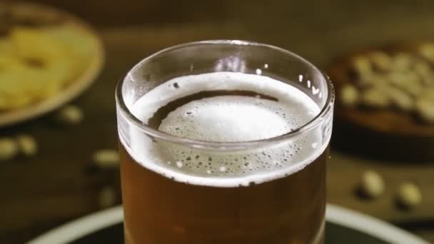 Schuimend koud licht bier in een glazen mok op een houten tafel draait in een cirkel. — Stockvideo