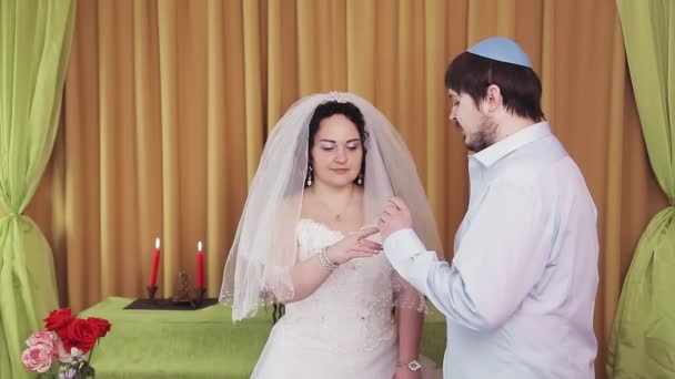 Durante la ceremonia de chuppah, una novia y un novio judíos en una sinagoga ponen un anillo en el dedo índice de las novias. — Vídeos de Stock