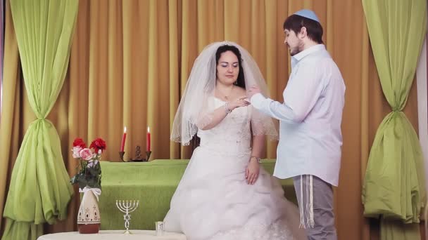 During the chuppah ceremony, a Jewish bride and groom in a synagogue puts a ring on the brides index finger — Stock Video