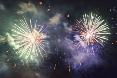 Dumanın içindeki karanlık gökyüzüne karşı parlak mor havai fişekler. Yatay fotoğraf