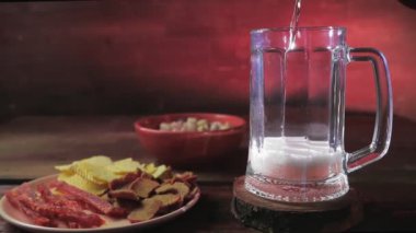 Şam fıstığı ve cipsin yanındaki masaya köpüklü soğuk bir bira dökülüyor.