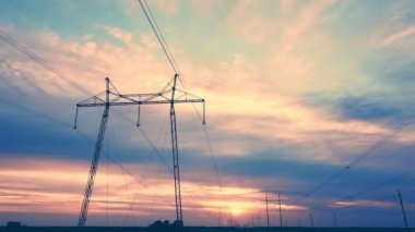 Açık bir alanda, batan güneşin arka planına karşı yüksek voltajlı elektrik hatları.