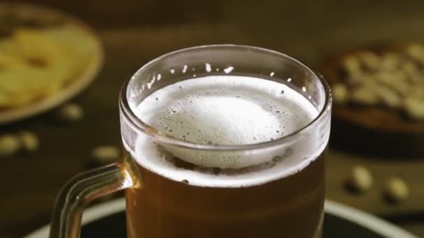 Schäumend kaltes, leichtes Bier im Glaskrug auf einem Holztisch dreht sich im Kreis — Stockvideo