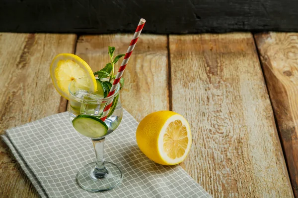 Коктейль з огірком вода з лимоном і м'ятою в склянці на серветці на чорному тлі біля лимона та огірка . — стокове фото