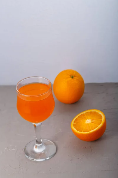 Orange juice in a glass near oranges on a gray background. — Stock Photo, Image