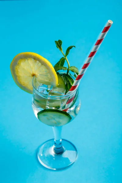 Коктейль з огірковою водою з лимоном та м'ятою у склянці на серветці на синьому фоні . — стокове фото