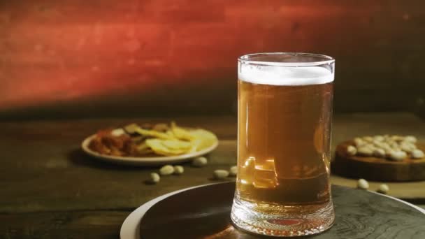 Піноутворення холодного легкого пива в скляній чашці на дерев'яному столі з закускою обертається в колі — стокове відео
