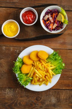 Peynir sosunun yanında tavuk nuggetlı patates kızartması ve ahşap bir masada et suyu teknesinde ketçap..