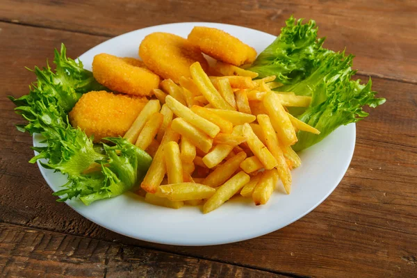 French fries with chicken nuggets in a plate with salad on a wooden table. — Stock Photo, Image