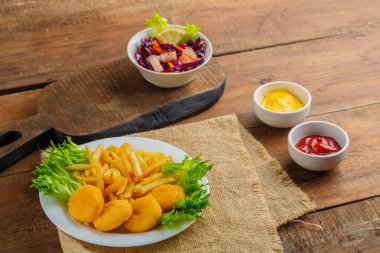 Patates kızartması, ahşap bir masanın üzerindeki peçetenin yanında soslu tavuk nugget. Yatay fotoğraf