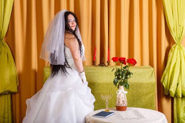 Duvağı olan beyaz gelinlikli Yahudi bir gelin, törenden önce çiçeklerle dolu bir masada ayakta duruyor. Yatay fotoğraf
