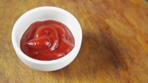 El ketchup de tomate en un bote de salsa blanca sobre un fondo de madera gira en círculo — Vídeo de stock