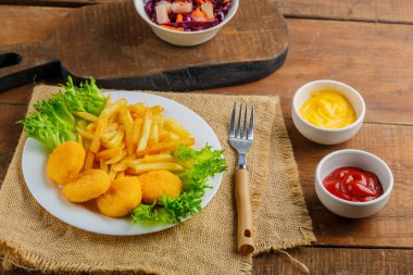 Patates kızartması, ahşap bir masanın üzerindeki peçetenin yanında soslu tavuk nugget. Yatay fotoğraf