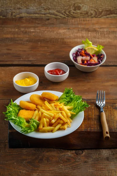Peynir sosunun yanında tavuk nuggetlı patates kızartması ve ahşap kalasların üzerinde sos kabında ketçap. Dikey fotoğraf