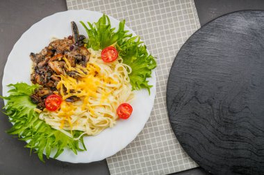 Mantarlı bir tabak makarna ve peçetedeki gri beton arka planda otlarla süslenmiş peynir. Yatay fotoğraf