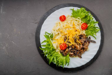 A plate of pasta with cheese and mushrooms decorated with herbs on a gray background. copy space. Horizontal photo
