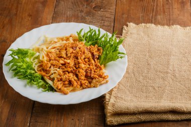 Keten peçetenin yanındaki ahşap masada otlarla süslenmiş bir tabak bolonez makarna. Yatay fotoğraf