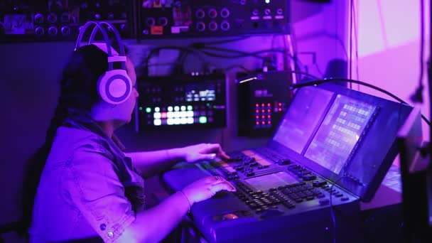 Inżynier oświetlenia w słuchawkach steruje urządzeniami oświetleniowymi na scenie przy pilocie w pomieszczeniu oświetleniowym. — Wideo stockowe