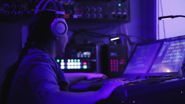 Inżynier oświetlenia kobieta ze słuchawkami przy konsoli kontroluje urządzenia oświetleniowe — Wideo stockowe