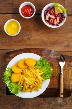 Peynir sosunun yanında tavuk nuggetlı patates kızartması ve ahşap bir masada et suyu teknesinde ketçap..