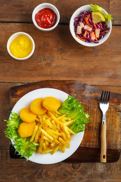 Peynir sosunun yanında tavuk nuggetlı patates kızartması ve ahşap bir masada et suyu teknesinde ketçap..
