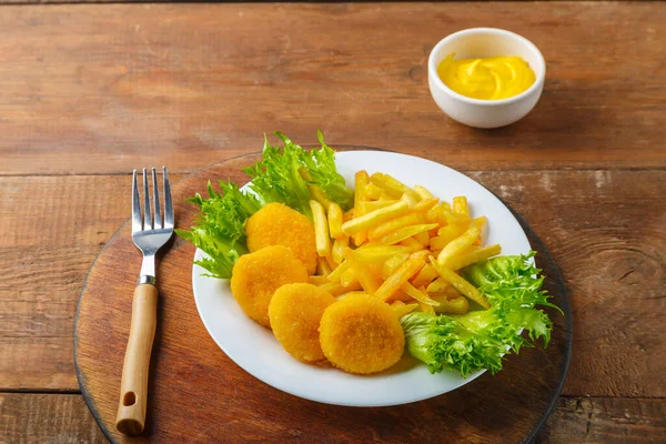 Patates kızartması, tavuklu nugget tabakta, ahşap bir masada peynir sosunun yanında. Yatay fotoğraf