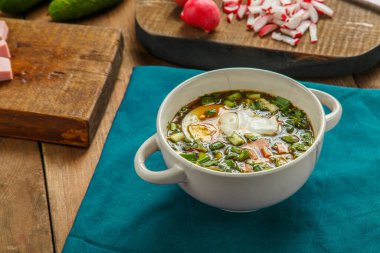 Sebzelerin yanındaki mavi peçetenin üzerinde kvass tablasıyla Okroshka. Yatay fotoğraf