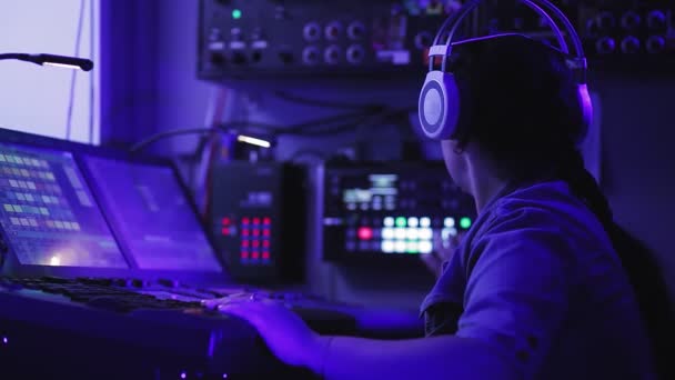 Una mujer diseñadora de iluminación con auriculares en la consola controla las luces. — Vídeos de Stock