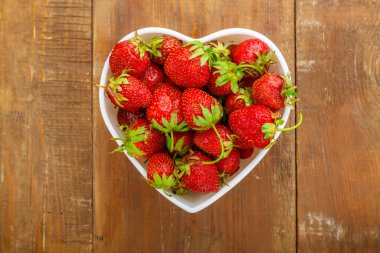 Tahta bir arka planda, kalp şeklinde bir tabakta taze çilekler..