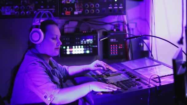 Inżynier oświetlenia w słuchawkach steruje urządzeniami oświetleniowymi na scenie przy pilocie w pomieszczeniu oświetleniowym — Wideo stockowe