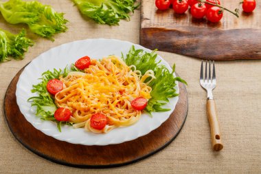 Bir tabak makarna, kiraz domatesli ve peynirli, bir çatalın yanındaki ahşap tezgahta..