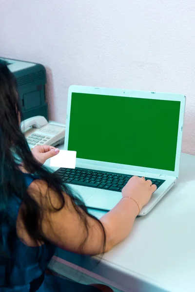 Uma mulher morena em seu escritório em casa faz compras na Internet pagando com um cartão de crédito on-line tela verde. — Fotografia de Stock