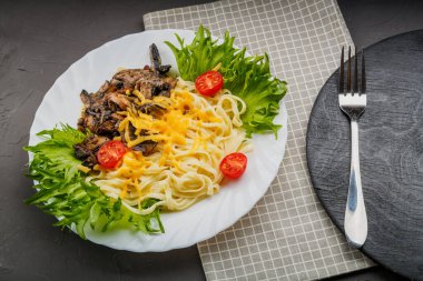 Çatalın yanındaki gri arka planda otlarla süslenmiş peynirli ve mantarlı bir tabak makarna. kopyalama alanı. Yatay fotoğraf