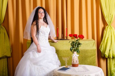 Duvağı olan beyaz gelinlikli Yahudi bir gelin Chupa seremonisinden önce çiçeklerle dolu bir masada duruyor. Yatay fotoğraf