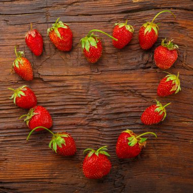 Tahta bir masanın üzerine kalp şeklinde serilmiş taze büyük çilekler..