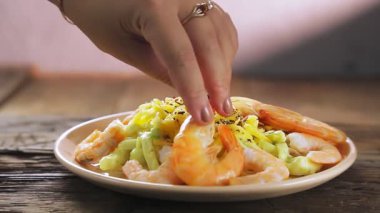 Bir kadın makarnayı kremalı soslu ve peynirli karideslerle süslüyor.