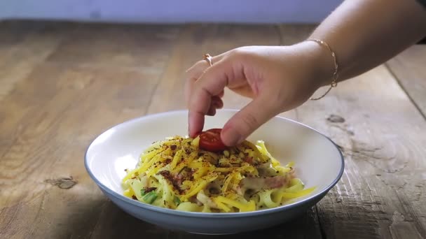 Egy női kéz cseresznyés paradicsommal díszíti a carbonara pasztát egy tányéron. — Stock videók