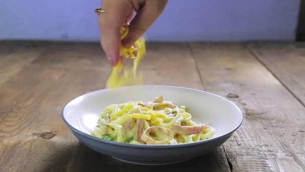 Sebuah tangan wanita memercikkan keju parmesan pada pasta karbonara di piring — Stok Video