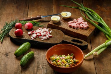 Okroshka kil bir tabakta, tahta bir masanın üzerinde yumurta sosisi ve salatalıkların yanında. Yatay fotoğraf