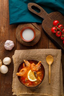 Tom yer elması çorbası, karides ve hindistan cevizi sütüyle sebze ve ahşap kaşığın yanındaki keten peçetenin üzerinde. Dikey fotoğraf