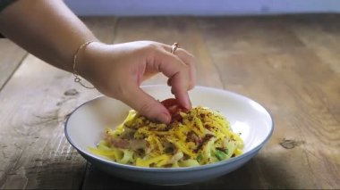 Bir kadın eli, carbonara ezmesini bir tabakta kiraz domatesiyle süslüyor.