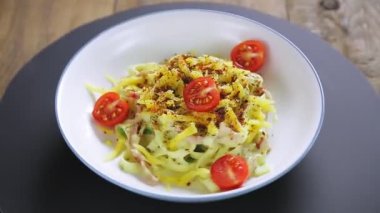 Kremalı carbonara soslu makarna ve tabakta dönen baharatlar siyah bir standın üzerinde daireler çiziyor..