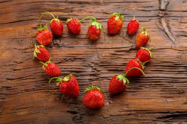 Ahşap arka planda taze çilekler kalp şeklinde serilmiştir..
