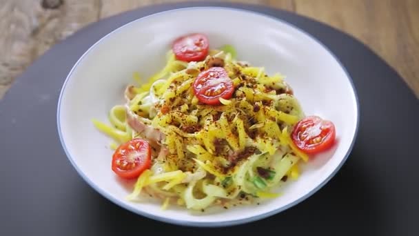 La pasta en una salsa carbonara cremosa y especias en un plato gira en círculo sobre un soporte negro — Vídeo de stock