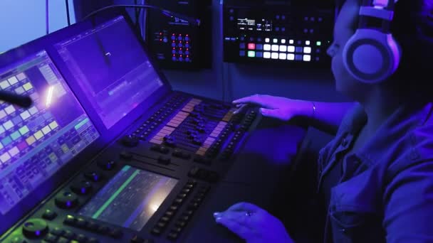 A female engineer illuminator in headphones controls the lighting devices on the stage at the console — Stock Video