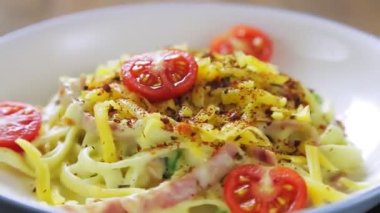 Kremalı karbonara soslu makarna siyah bir stantta bir tabakta daire şeklinde döner.