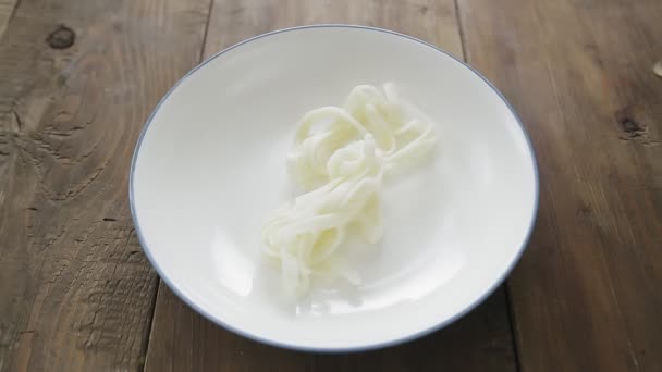 Tongs menempatkan udon di piring di atas meja kayu — Stok Video