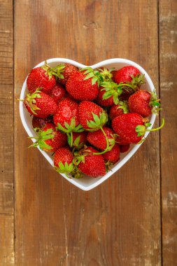 Kalp şeklinde bir tabakta taze büyük çilekler. Dikey fotoğraf