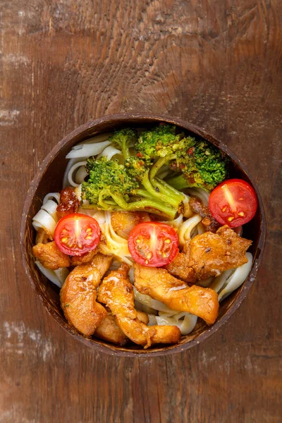 Udon con pollo en salsa japonesa en un plato de cáscaras de coco en una mesa de madera. — Foto de Stock